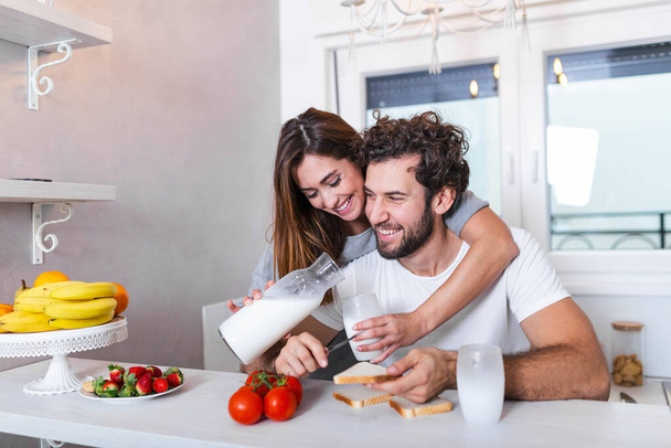 Романтическая молодая пара готовит вместе на кухне, отлично проводит время вместе. Мужчина и женщина смеются и пьют молоко утром с завтраком - Фото, изображение