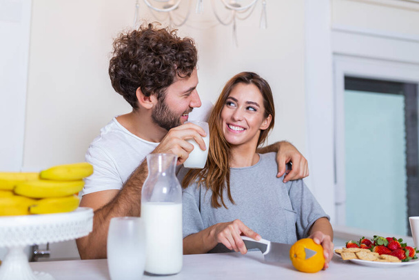 Молодая пара вместе готовит еду на кухне, весело проводит время вместе. Мужчина и женщина смеются и пьют молоко утром с завтраком - Фото, изображение