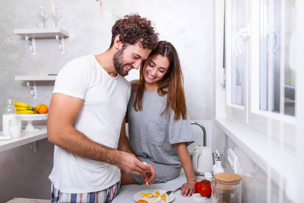 Portrait of happy young couple cooking together in the kitchen at home. romantic Attractive young woman and handsome man are enjoying spending time together while standing on light modern kitchen. - Foto, afbeelding