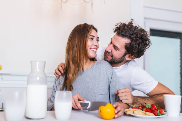 happy young couple have fun in modern kitchen indoor while preparing fresh fruits and vegetables food salad. Beautiful young couple talking and smiling while cooking healthy food in kitchen at home. - Photo, Image