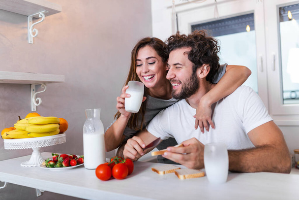 glückliches junges Paar vergnügt sich in der modernen Küche drinnen, während es frischen Obst- und Gemüsesalat zubereitet. Schönes junges Paar plaudert und lächelt beim Kochen gesunder Lebensmittel in der heimischen Küche. - Foto, Bild