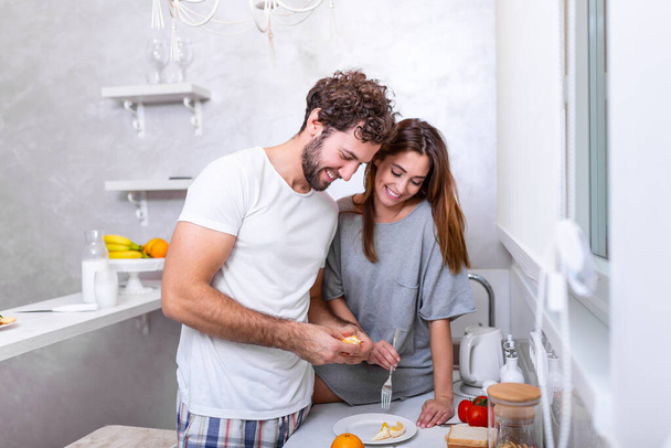 Female and male vegeterians stand together against kitchen interior, prepare fruit salad. Family couple cook on cozy kitchen, husband helps young wife to preapre breakfast for whole family. - Фото, изображение