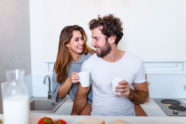 Ρομαντικό ζευγάρι ερωτευμένο να περνάει χρόνο μαζί στην κουζίνα. Χαριτωμένο νεαρό ζευγάρι πίνοντας καφέ στην κουζίνα και απολαμβάνοντας την πρωινή ώρα μαζί - Φωτογραφία, εικόνα