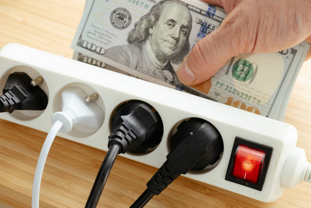 Αυξήσεις στις τιμές της ηλεκτρικής ενέργειας στις Ηνωμένες Πολιτείες, Ενέργεια έννοια, Power strip με βύσματα στην πρίζα και ένα μεγάλο πακέτο δολάρια στο χέρι, Αύξηση των τιμών της ενέργειας για τα νοικοκυριά και τη βιομηχανία - Φωτογραφία, εικόνα
