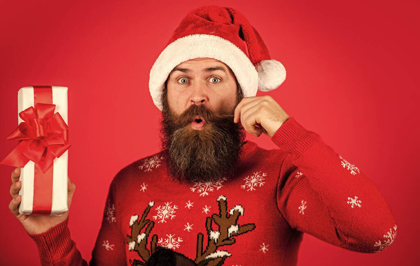 Jingle bells. winter holiday party. mature guy celebrate new year. bearded hipster in xmas sweater. surprised man with beard in santa claus hat. brutal man hold present box. christmas online shopping. - Foto, imagen