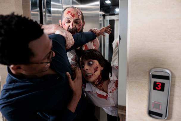 Aggressive eerie zombies attacking afraid man, leaving elevator and hunting person to eat brain. Scared adult running from horror terrifying evil monsters, walking dead sinister corpses. - Foto, imagen