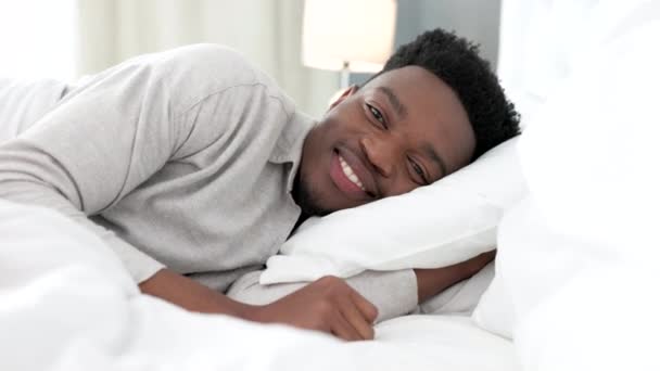 Slaap, bed and man portret in de slaapkamer in een luxe hotel voor vakantie of vakantiehuis in de ochtend. Glimlach van een zwarte man liggend op kussen voor comfortabel meubilair, beddengoed of nieuw appartement. - Video