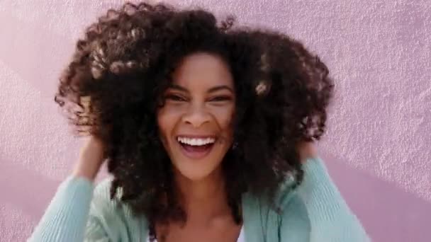 Retrato de mujer negra tocando su afro al aire libre por una pared rosa mientras abrazaba sus rizos. Chica feliz, latina y tonta abrazando su cabello natural con un cuidado del cabello, bienestar y estilo de vida de belleza - Metraje, vídeo