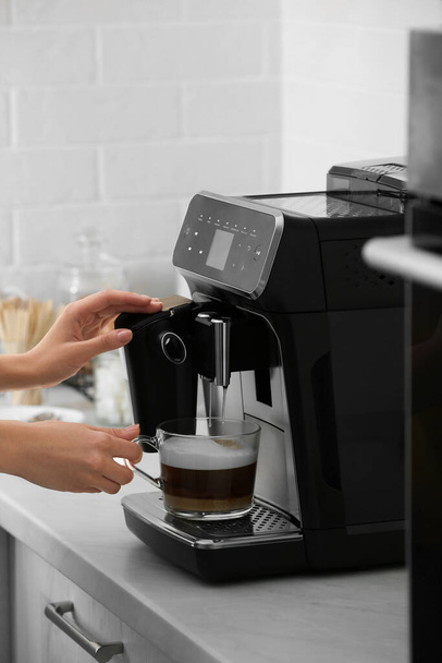 Woman using modern espresso machine for making coffee with milk in kitchen, closeup - Foto, afbeelding
