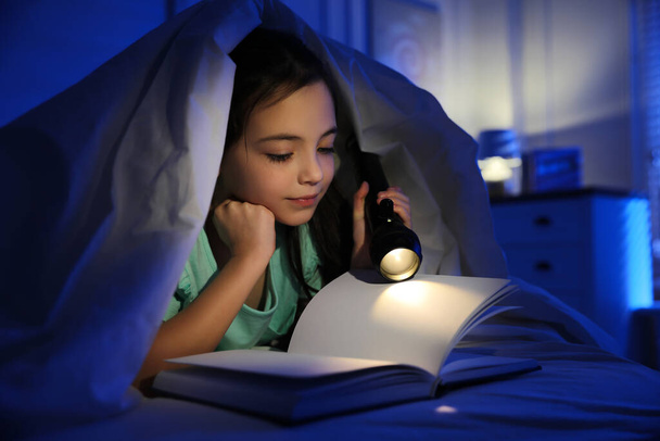 Little girl with flashlight reading fairy tale in dark bedroom - Fotó, kép