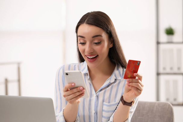 Woman with credit card using smartphone for online shopping indoors - Foto, Imagen