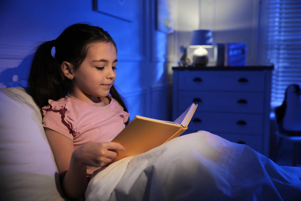 Little girl reading fairy tale in dark bedroom - Фото, изображение