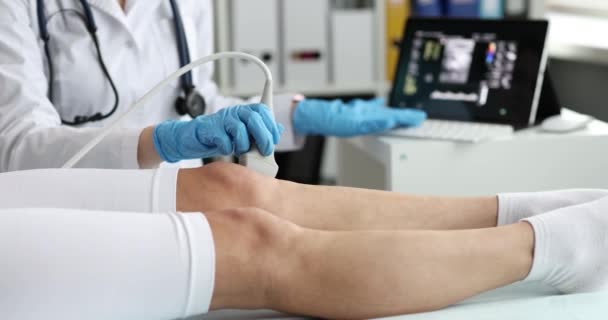 Le médecin fait une échographie de l'articulation du genou à la femme en utilisant un échographe à la clinique. Le docteur passe une sonde à ultrasons sur la jambe d'une femme à l'hôpital - Séquence, vidéo