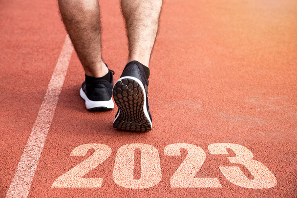 Ziele und Pläne für das nächste Jahr. Rückansicht eines Mannes, der sich auf einen Start auf einer Leichtathletikbahn vorbereitet, eingraviert mit dem Jahr 2023 - Foto, Bild