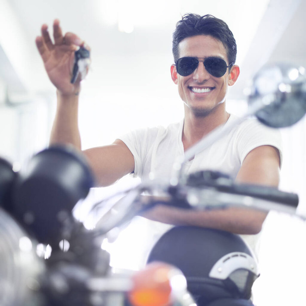 Valmiina hauskanpitoon. Komea nuori mies istuu moottoripyörällään pitäen sen avaimia. - Valokuva, kuva