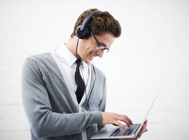 Managing his playlist. A handsome young nerd with headphones working on his laptop - Photo, Image