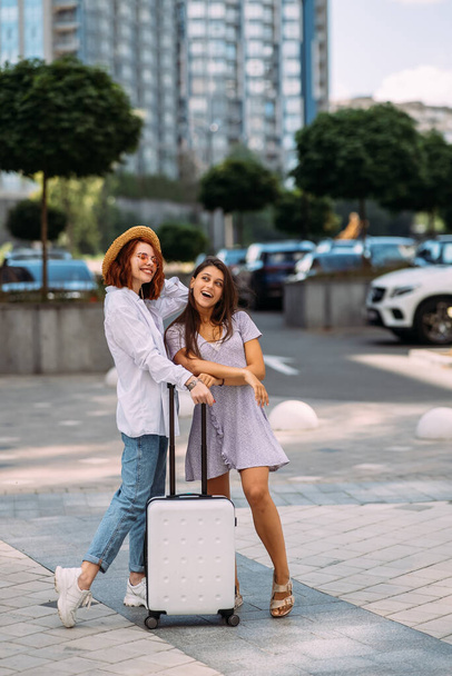 Две молодые женщины с чемоданом позируют перед камерой на улице - Фото, изображение