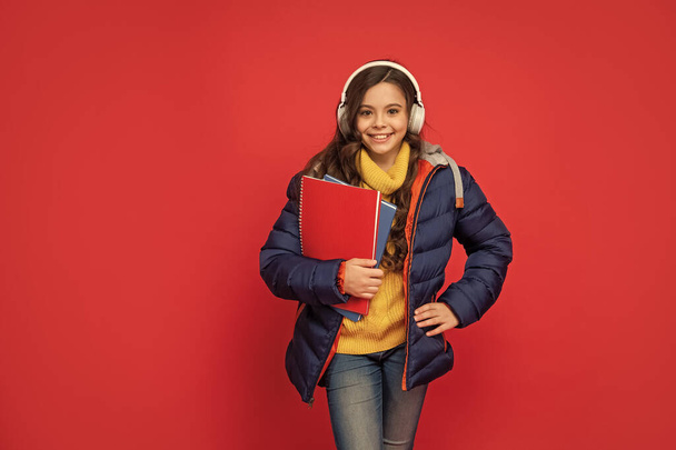 back to school. happy child listen music in headphones hold book. kid wear warm clothes. express positive emotion. winter fashion. teen girl in hat and earphones. modern life in childhood. - Foto, Imagem