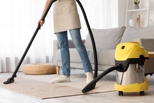 Jeune femme au foyer nettoyage tapis avec aspirateur à la maison - Photo, image
