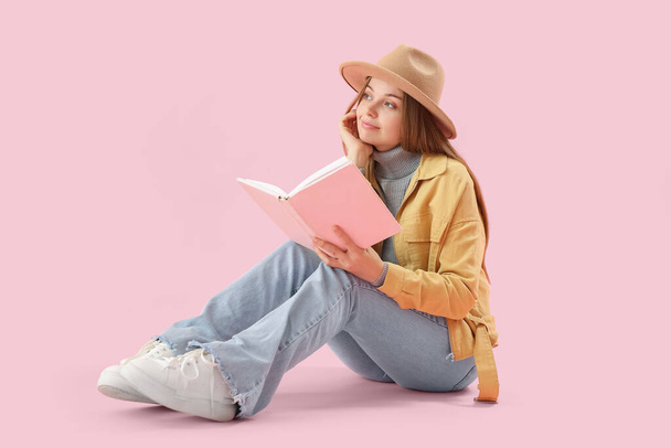 Young woman with book sitting on pink background - Photo, image
