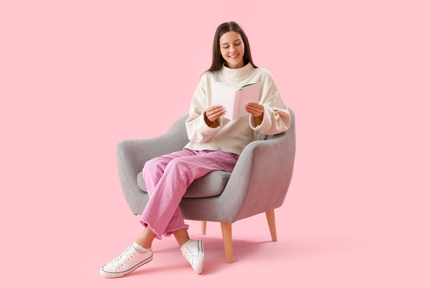 Hermosa mujer leyendo libro en sillón sobre fondo rosa - Foto, Imagen