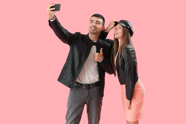 Fashionable couple in autumn clothes taking selfie on pink background - Photo, Image