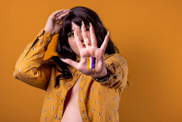 Junge nicht-binäre Frau mit nicht-binärer Geschlechterfahne in der Hand. Orange Hintergrund. - Foto, Bild