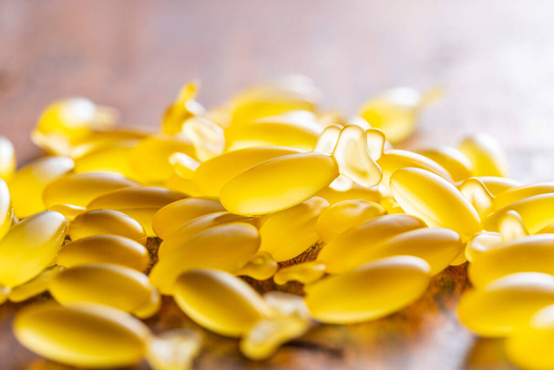 Fish oil capsules. Yellow omega 3 pills on the wooden table. - Foto, Imagem