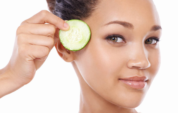 Nature is at the heart of skincare. Closeup of a gorgeous young woman holding a slice of cucumber to her face - 写真・画像