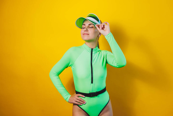 Söpö hoikka nainen kirkkaan vihreässä uimapuvussa ja aurinkohattu keltaisella taustalla. Kesäloma. Kokoelma naisten uimapuvut - Valokuva, kuva