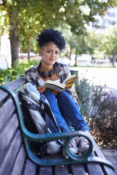 Relajado y disfrutando del aire exterior. Un estudiante sentado en un banco leyendo un libro - Foto, Imagen