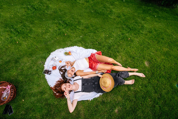 Two women having picnic together, laying on the plaid on the lawn - Foto, Imagem