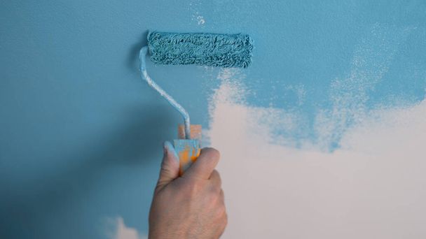 Ζωγράφος σπίτι ζωγραφίζει τοίχο μπλε με ρολό closeup. Επισκευή και βαφή τοίχων έννοια - Φωτογραφία, εικόνα