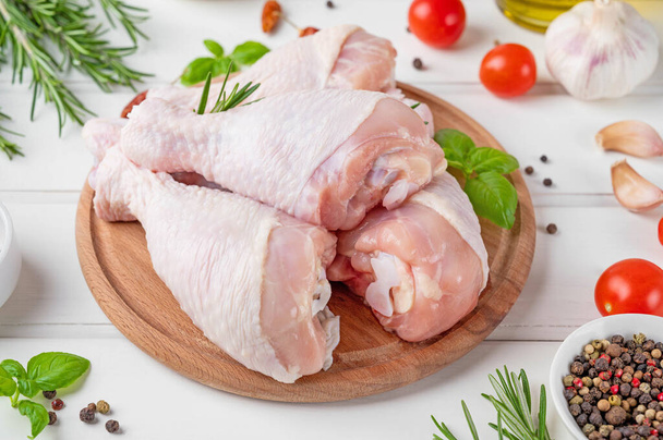 Raw uncooked chicken legs on a cutting board on a white wooden background. Meat with ingredients for cooking. - 写真・画像