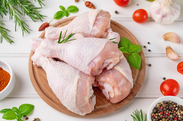 Pernas de frango crus não cozidas em uma tábua de corte em um fundo de madeira branco. Carne com ingredientes para cozinhar. - Foto, Imagem