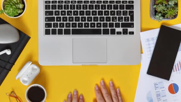 Mãos de mulher de negócios digitando no laptop vista superior sobre mesa de escritório amarelo. Trabalhando em relatórios trimestrais com xícara de café. Smark trabalhando em casa. Interrupção - Filmagem, Vídeo