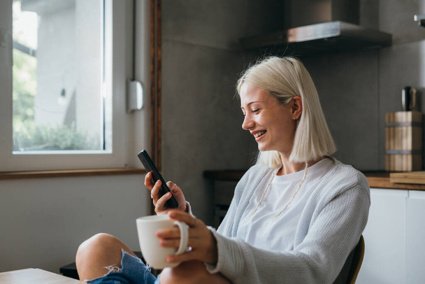 gen z female texting on her mobile phone and drinking morning coffee at home - Foto, Bild