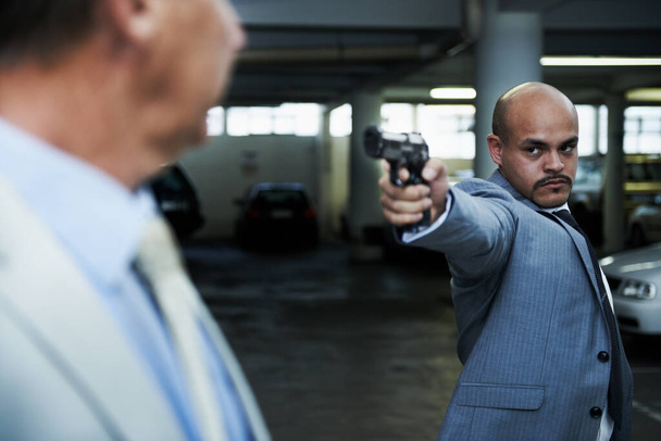 Viens avec moi et viens tranquillement. Un gangster en colère pointant son arme de poing sur un homme d'affaires choqué dans un parking sombre - Photo, image