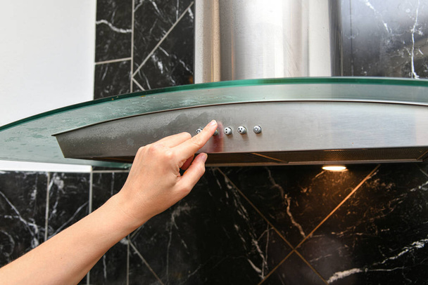 Uma mulher liga um capuz de cozinha para remover fumaça e maus cheiros da cozinha. - Foto, Imagem