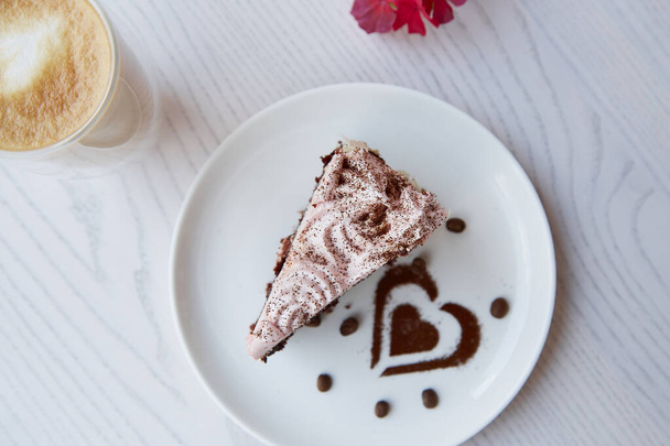 Esztétikai gyümölcs csokoládé torta és egy pohár dupla fenekű latte a fa asztal szabadban. Rózsaszín virágok dekoráció a kávézó teraszán. Légköri reggeli. Felülnézet. - Fotó, kép