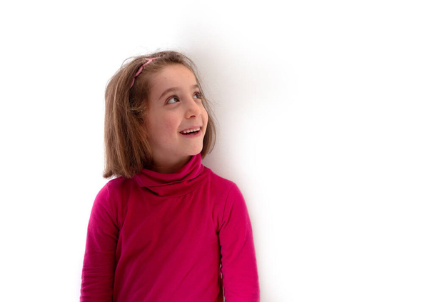 Pieni lapsi tyttö yllään punainen poolo kaula tai rulla-kaula hymyillen ja katsoen ylös valkoisella taustalla - Valokuva, kuva