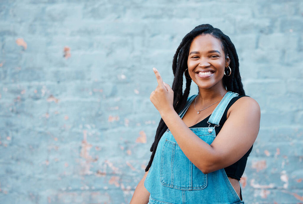 Schwarze Frau, Portrait und zeigt auf eine Hintergrundmockup-Wand für Werbung, Marketing-Nachrichten und Ankündigungen in städtischen Städten im Freien. Glücklich, lächelnd und junges Hipster-Mädchen werben für Botschaft. - Foto, Bild