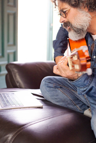 Vousatý muž se učí hrát na akustickou kytaru online z domova - Fotografie, Obrázek