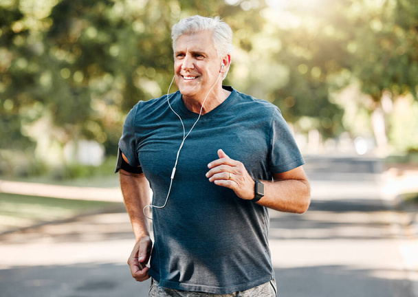 Senior man running while listening to music outdoor street and park for fitness, wellness or healthy lifestyle with summer lens flare bokeh. Elderly person exercise, workout or jogging with earphones. - Photo, Image