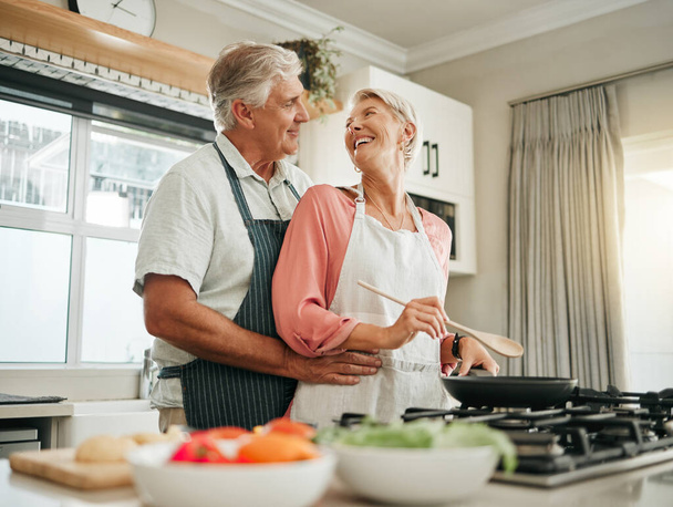 Senior couple, cooking and home bonding for fun, romance and happiness with husband hugging happy wife with love, care and offering help in the kitchen. Food, marriage and joy with old man and woman. - Zdjęcie, obraz