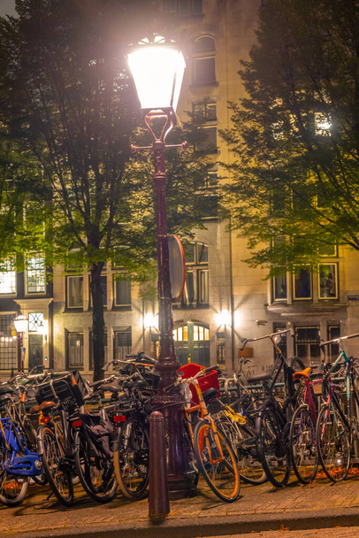 Netherlands. Summer night in Amsterdam. Lots of parked bikes under a street lamp on the canal embankment - Foto, Imagem