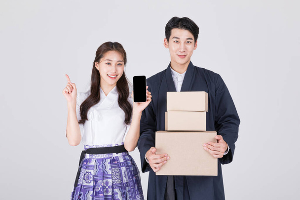 Korean couple, young man and woman in 20s, wearing modern Hanbok, holding smartphone and delivery box - Foto, immagini