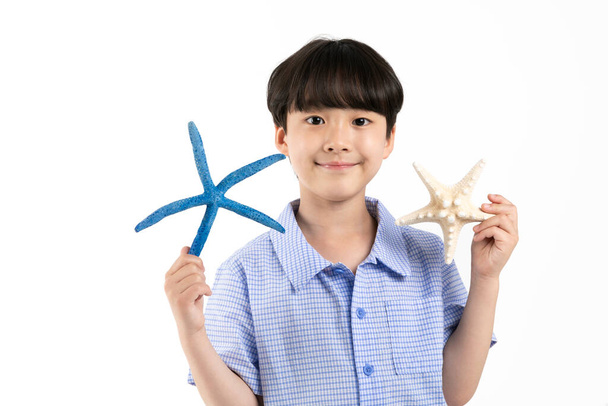 Korean young boy wearing summer blue half sleeve shirt in white background studio_holding a starfish - Fotografie, Obrázek