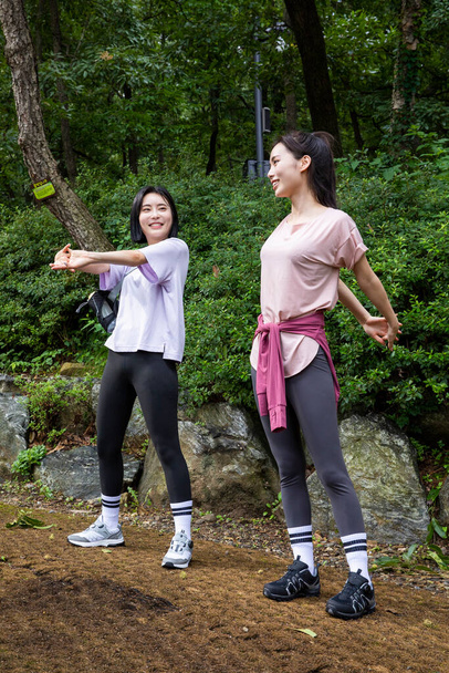 two Korean Asian female friends in 20s hiking and plogging in mountain__warm up - Foto, Bild