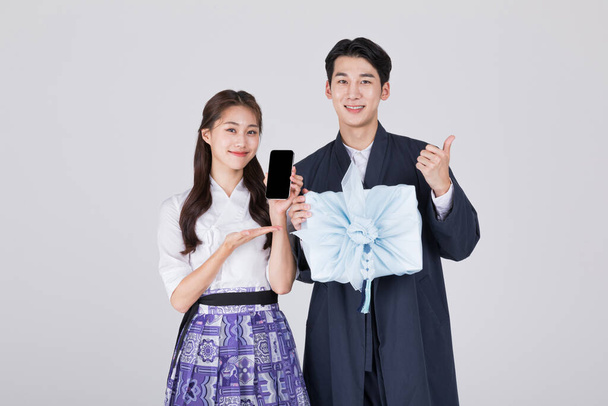 Korean couple, young man and woman in 20s, wearing modern Hanbok, holding traditional box and smartphone - Fotografie, Obrázek